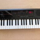 Černý přenosný digitální klavír s bílými a černými klávesami. Na levé straně je bílý nápis YAMAHA a model PSS-A50. Přístroj má ovládací panel s různý…