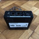 Zadní strana černého efektového pedálu s různými konektory. Jsou zde nápisy POWER, OUTPUT, THRU, IN INST, GRND a MIC INPUT. Na spodní části je štítek…