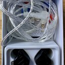 V bílém boxu jsou umístěny černé sluchátka typu in-ear s nápisem HYBRID TECHNOLOGY. K nim je přiložen dlouhý, průhledný kabel s konektory. V pozadí j…