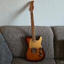 Elektrická kytara s tělem v provedení sunburst a zlatým pickguardem. Hmatovnice je z tmavého dřeva s viditelnými pražci a hlava kytary je v přirozené…