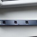 Detail zadní strany tmavého rackového zařízení s čtyřmi výstupními konektory XLR. Nad konektory jsou bílé nápisy OUTPUT D, OUTPUT C, OUTPUT B a OUTPU…