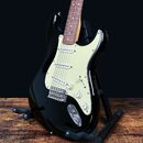 Černá elektrická kytara typu Stratocaster s bílým pickguardem a hnedým hmatníkem. Nástroj má tři snímače s bílými krytkami, jeden přepínač a tři ovlá…