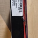 Fotografie zachicuje balení s červeným příslušenstvím, pravděpodobně strunami. Na bílé nálepse je čárcový kód a text: ORIGINAL J BASS SET OF 2, P.N.…