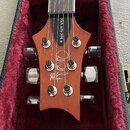 Fotografie zachycuje hlavu elektrické kytary v červeně vyloženém kufru. Na dřevěné hlavě jsou vidět nápisy „McCarty 594“, logo „Paul Reed Smith“ a oz…