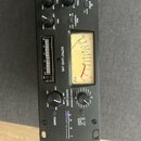 Černý rackový audio procesor s analogovým VU metrem. Na panelu jsou nápisy OUTPUT LEVEL (dB), SAMPLE RATE/OTHER, OUTPUT LEVEL -3dB 0 +3dB a POWER. V…