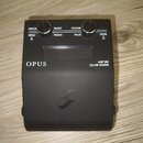 Černý kytarový efekt s nápisy OPUS a AMP SIM DynIR ENGINE. Zařízení má dva ovládací knoflíky a tlačítka s popisky PERFOR., PRESET, VOLUME, MENU, PARA…