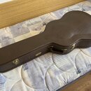 Hnědý tvrdý kufr na kytaru s texturovaným povrchem a světlými švy po obvodu. Na boku je umístěno zlaté logo s nápisem "Gretsch". Kufr má kovové zámky…