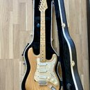 Elektrická kytara s přírodním dřevěným povrchem těla a hmatníkem z jasného dřeva. Na hlavě je viditelné logo Fender. Kytara má perleťový pickguard, t…