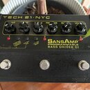 Černý kytarový pedál s nápisem TECH 21 NYC a SansAmp PROGRAMMABLE BASS DRIVER DI. Horní panel obsahuje šest černých otočných potenciometrů s popisky…