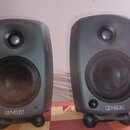 Dva šedé studiové monitory s kovovými mřížkami přes basové reproduktory. Na spodní části obou přístrojů je bílý nápis GENELEC. Reproduktory stojí na…