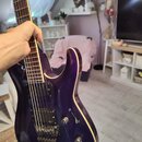 Elektrická kytara s tmavě fialovým lakem a viditelným dřevěným lemováním kolem korpusu. Nástroj má dva humbuckery, ovládací knoflíky a vibrační systé…
