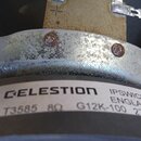 Detail reproduktoru s bílou nálepkou, na které je černý nápis CELESTION IPSWICH ENGLAND G12K-100 27 FN 8Ω T3585. Kovový rám je stříbrný, vykazuje výr…