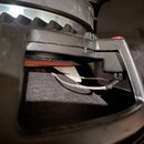 Detailní pohled na zadní část černého reproduktoru. Je vidět kovový rám a připojovací vodiče vedoucí k cívce. Na povrchu rámu jsou vidět drobné prach…