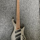 Stříbrná elektrická basa s šesti strunami a hnědým hmatníkem. Na korpusu je viditelné logo Ibanez. Nástroj má černý hardware a tři ovládací knoflíky…