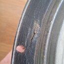 Detailní pohled na okraj černého, pravděpodobně dřevěného, kulatého hudebního nástroje nebo příslušenství. Povrch je výrazně opotřebovaný, s viditeln…