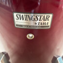 Detail červeného bubnu s nalepeným stříbrným štítkem. Na štítku je uveden nápis SWINGSTAR by TAMA a text MADE IN TAIWAN R.O.C. V levé části štítku je…