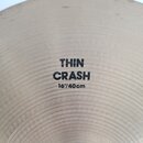 Detailní záběr na povrch kovového činely. Uprostřed je černý nápis THIN CRASH a pod ním 16"/40cm. Povrch vykazuje jemné koncentrické rýhy.