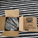 Kartonová krabice s černým reproduktorem zabaleným v průhledném plastovém sáčku. Na vnitřní straně víka je logo GRS a nápis REPLACEMENT SPEAKERS. Ští…