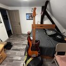Elektrická basová kytara s hnědým průsvitným lakem na těle a dřevěným hnedým krkem. Na hlavě nástroje je viditelné logo Fender. Basgitara má červený…