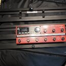 Černý kovový rack, v němž je osazen červený přístroj s nápisem BOSS RC-600 LOOP STATION. Zařízení má displej, několik ovládacích knoflíků a tlačítek.…
