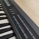 Detailní pohled na ovládací panel a klávesy elektronického nástroje v černé barvě. Na panelu jsou šedé tlačítka a nápisy: GROUP, PRESET, MEMORY, CART…