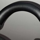 Detailní záběr na černý, polstrovaný oblouk sluchátek z materiálu připomínajícího kůži. Povrch je hladký a bez viditelných poškrábání či opotřebení.…