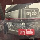 Fotografie zobrazuje krabici a plastový obal s manuálem k wah-wah pedálu. Na krabici je černobílá fotografie přístroje s nápisem cry baby. V plastové…