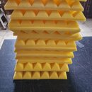 Stoh žlutých akustických absorbů z pěny s pyramidovým povrchem. Panely jsou naskládány na sebe na tmavém podkladu. Na fotografiích nejsou viditelné ž…