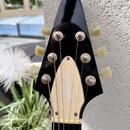 Černá hlava elektrické kytary s bílým plastovým krytem. Na krytu je nápis Gibson v kurzívě. Jsou vidět šest ladicích kol v krémové barvě a kovové mec…
