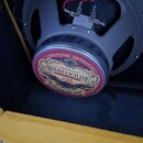 Zadní strana kytarového reproduktoru v šedém rámu s připojenými červeným a modrým kablem. Na kulatém štítku je nápis BRITISH INVASION a logo WAREHOUS…