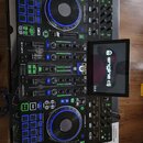 Černý DJ kontrolér Denon DJ Prime 4 s integrovaným displejem, na kterém je nápis engine dj a verze 5.0. Zařízení má dva jog-kola s modrým podsvícením…