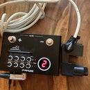 Černý ovládací modul s digitálním displejem, na kterém svítí červená číslice 2. Na zařízení je bílý nápis Roland a ovládací prvky s označením MUTE, +…