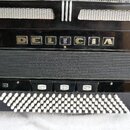 Černý akordeon s bílými knoflíky v dolní části. Na předním panelu je nápis DELICIA a vlevo menší nápisy CHORAL VI. Povrch je lesklý, v horní části js…