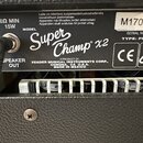 Detail zadní strany kytarového komba s černým texturovaným povrchem. Na černém štítku je bílý nápis MODEL Super Champ X2 a text A PRODUCT OF: FENDER…