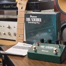 Na fotografii je zelený kytarový efekt pedál s nápisy Ibanez a TUBE SCREAMER Overdrive Pro TS808DX. Vedle pedálu je umístěna jeho originální krabice…