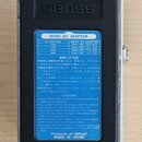 Zadní strana efektového pedálu značky BOSS v kovovém šasi. Uprostřed je modrá nálepka s nápisem BOSS AC ADAPTOR, tabulkou napětí a doporučenými adapt…