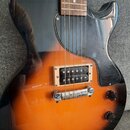 Elektrická kytara s tělem v oranžovo-černém sunburst provedení a černým plechtrátem. Nástroj má jeden humbucker dopusťovaný v krémovém rámečku a dva…