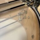 Detailní pohled na horní část bubnu s kovovým mechanismem snareho. Viditelný je chromovaný rám a pružinový mechanismus s vlnovitou strukturou. Tělo b…
