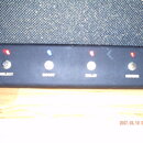 Černý obdélníkový ovladač s čtyřmi tlačítky a kontrolkami. Pod tlačítky jsou bílé nápisy SELECT, BOOST, DELAY a REVERB. Na levé straně je viditelný k…