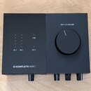 Černý audio rozhraní s matným povrchem. Na horní části jsou nápisy OUT 1/2 VOLUME, USB, 48 V a označení vstupů IN 1 a IN 2 u sloupců s kontrolkami. V…