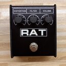 Černý efekt pedál s nápisem RAT v bílém obdélníku. V horní části jsou tři černé otočné ovladače s popisky DISTORTION, FILTER a VOLUME. Ve spodní část…