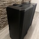 Dva černé reproduktory s kovovou mřížkou v přední části a integrovanou rukojetí na horní straně. Povrch je matně černý, v horní části je viditelný ne…