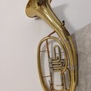 Mosazný železný nástroj typu horn s zlatavým povrchem. Na těle nástroje nejsou viditelné žádné značky, loga ani názvy modelů. Povrch vykazuje drobné…