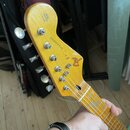 Hlava elektrické kytary v přírodním dřevě s nápisy Fender a STRATOCASTER. Na zadní straně hlavy je text ORIGINAL Contour Body. Povrch vykazuje známky…