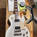 Bílá elektrická kytara typu Les Paul s hnědým hmatníkem a dvěma humbuckery. Na hlavě je viditelné logo Epiphone. Kytara má čtyři zlaté ovládací knofl…