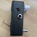 Fotografie zachycuje boční stranu černého kytarového pedálu. Jsou vidět dva vstupy: jeden menší kulatý konektor a jeden větší 6,35mm jack s kovovým p…