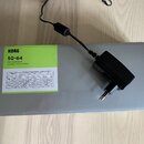 Šedá papírová krabice s nápisy KORG, SQ-64 a POLY SEQUENCER SÉQUENCEUR POLYPHONIQUE. Na krabici je vlepěná bílá schéma přístroje s nápisy KORG a SQ-6…