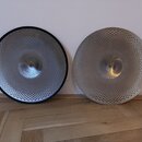 Dvě kovové činely s perforovaným povrchem v podobě malých otvorů. Levý činel má černý okraj, pravý činel je celkově stříbrný. Na obou nástrojích nejs…