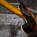 Detail spoje krku a těla elektrické kytary. Tělo má černý lak s přechodem do žlutohnědé barvy a krk je v žluté barvě. Na spoji je vidět kovovádeska s…