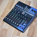 Kompaktní mixážní pult černé barvy s modrými bočními panely. Na přístroji je vidět logo YAMAHA a označení modelu MG10XU. Povrch obsahuje řadu potenci…